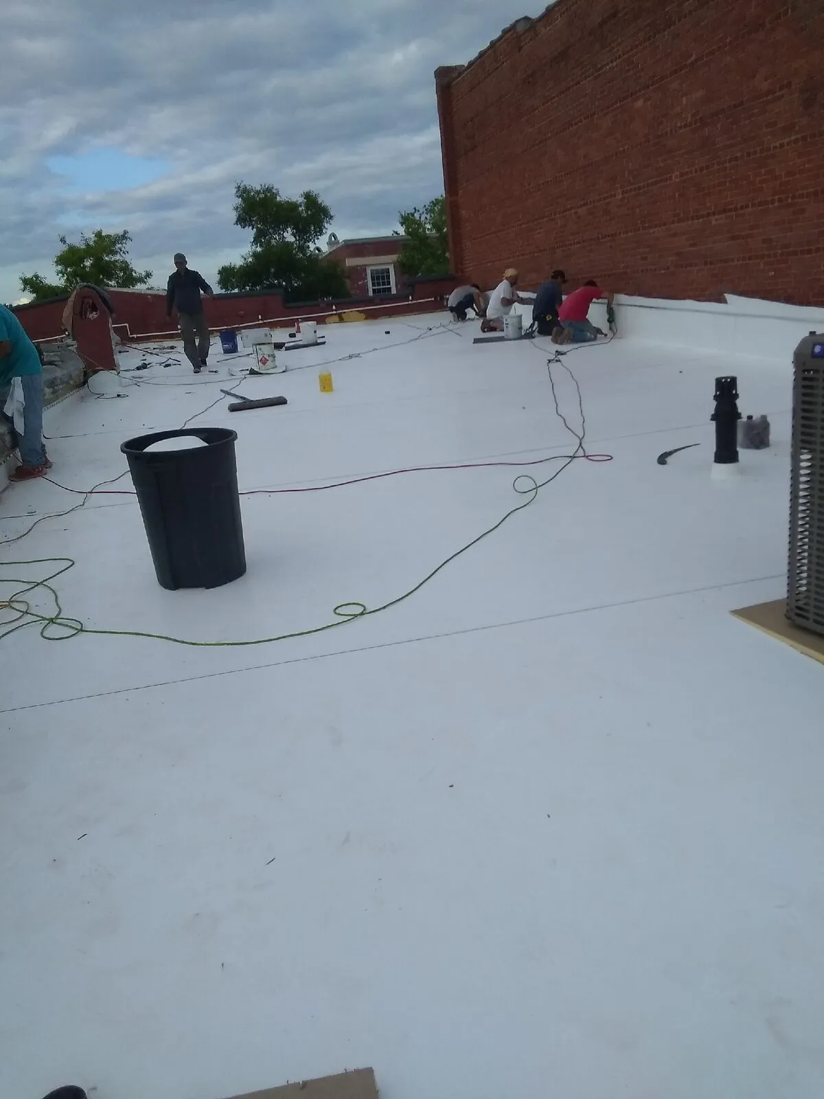 Crew installing white TPO membrane roofing on a downtown brick commercial building